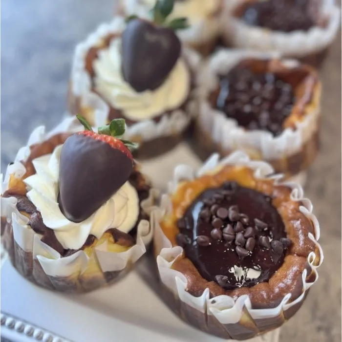 Mini cheesecake cups topped with whipped cream and a chocolate-covered strawberry