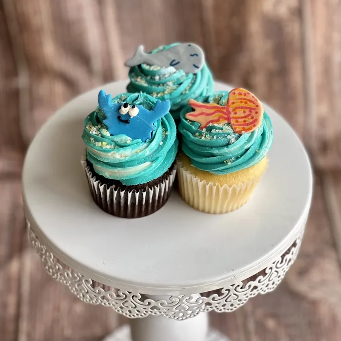 Cupcakes with teal swirled frosting topped with a fondant whale and fish
