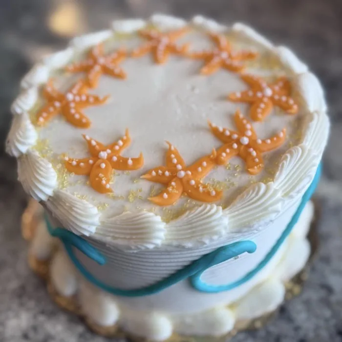 Elegant white wedding cake decorated with a ring of fondant starfish and a teal ribbon